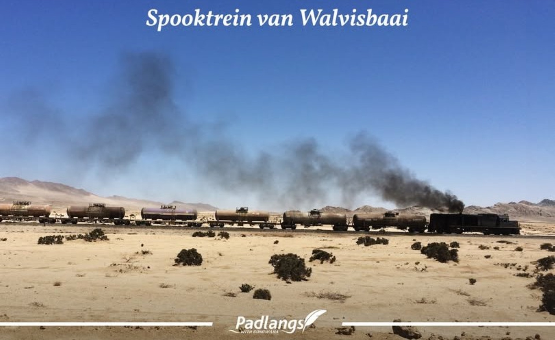 Derelict red locomotive lying on its side in Swakopmund after rolling unmanned from Walvis Bay, surrounded by onlookers.